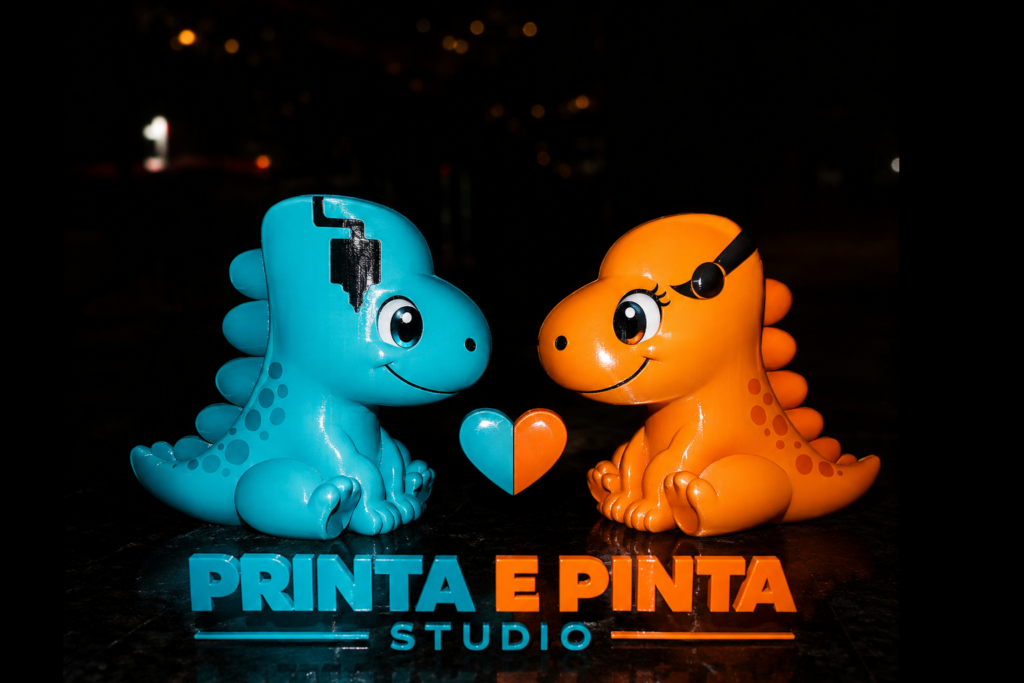 Dois dinossauros mascotes, um azul e outro laranja, sentados frente a frente com um coração bicolor ao centro e o nome Printa e Pinta Studio abaixo.